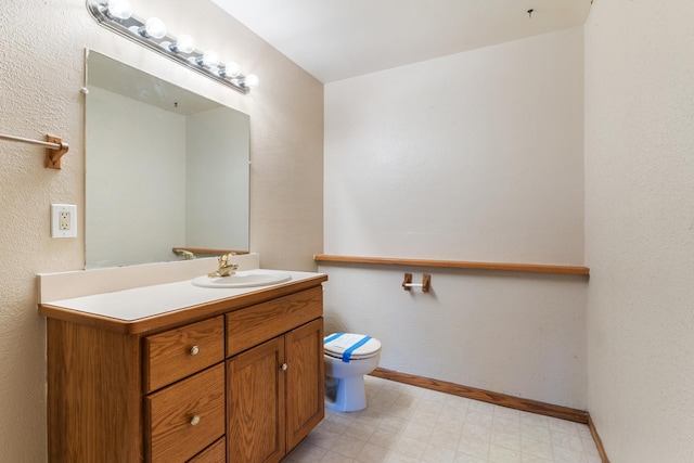 half bathroom with baseboards, vanity, toilet, and tile patterned floors