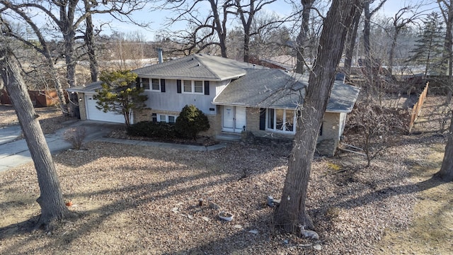 split level home featuring an attached garage, a shingled roof, concrete driveway, and brick siding