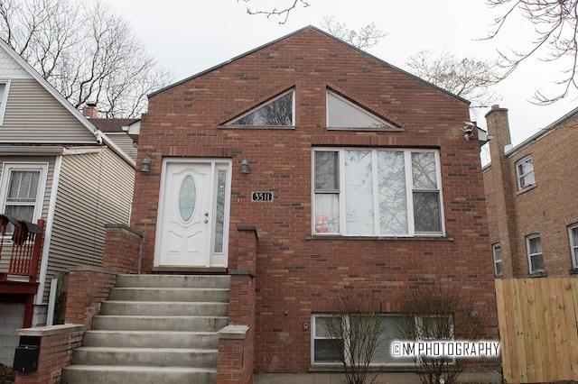 view of front of house with entry steps, brick siding, and fence