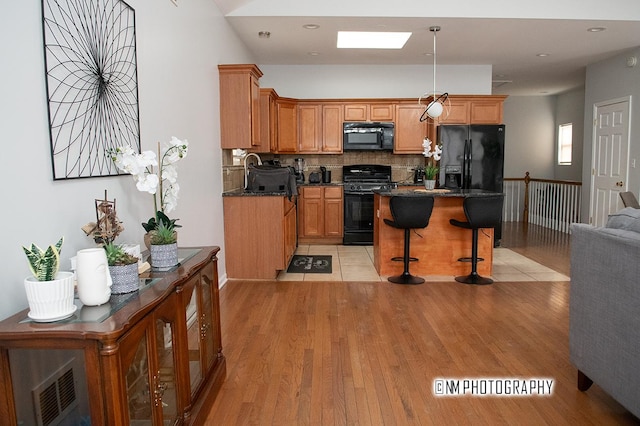 kitchen with a skylight, light wood-style floors, black appliances, a kitchen bar, and backsplash