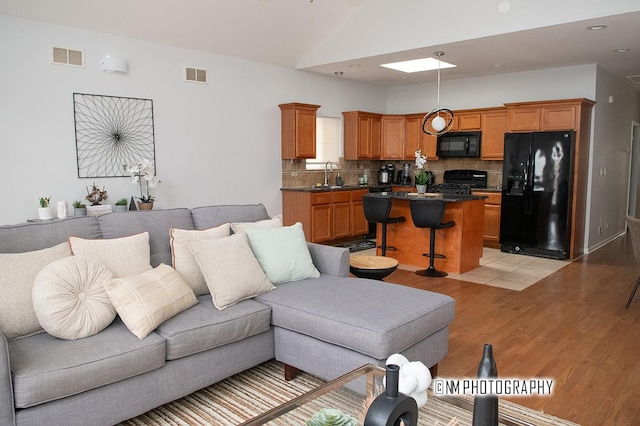 living area featuring light wood-style flooring, visible vents, and vaulted ceiling