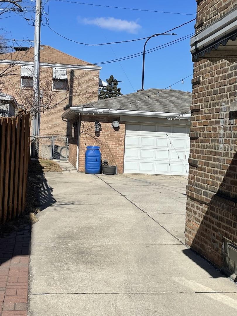 view of home's exterior with brick siding, a shingled roof, fence, a garage, and driveway