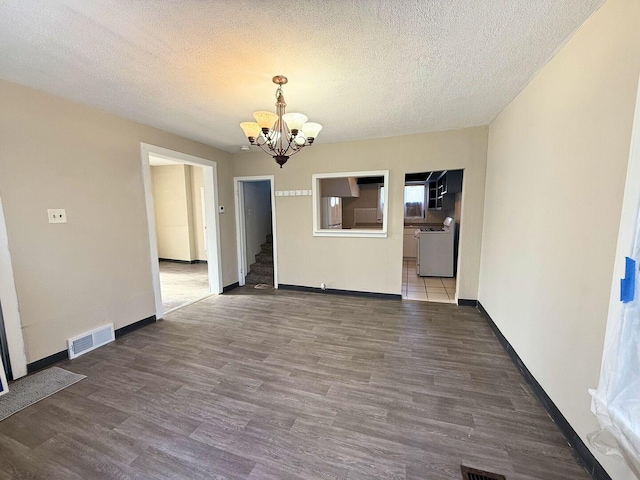 spare room with a textured ceiling, visible vents, a notable chandelier, and wood finished floors