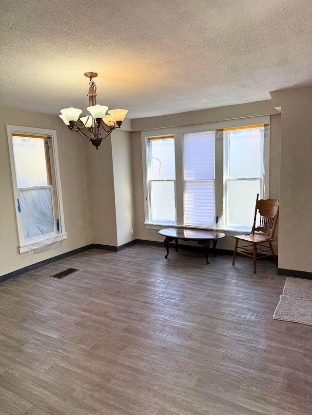 interior space featuring an inviting chandelier, a textured ceiling, baseboards, and wood finished floors