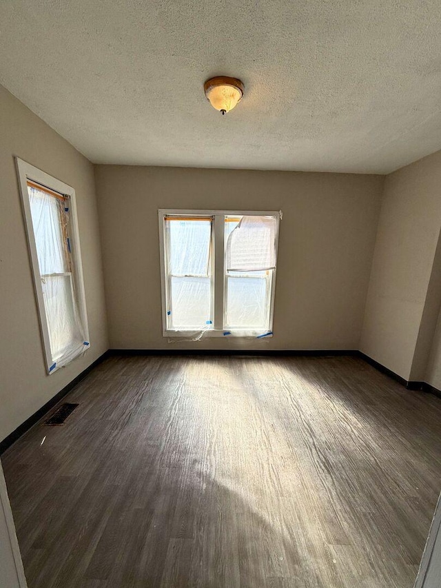 empty room featuring a textured ceiling, wood finished floors, visible vents, and baseboards