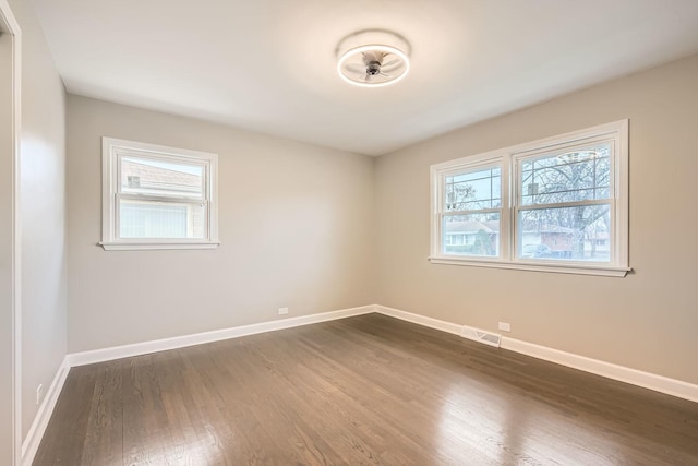 spare room featuring plenty of natural light, visible vents, baseboards, and dark wood-type flooring