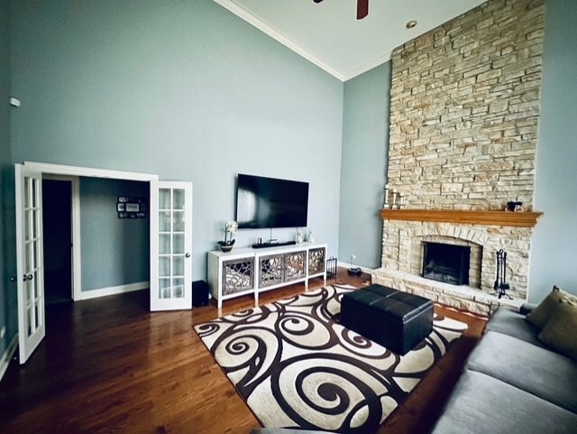 living room with a fireplace with raised hearth, ornamental molding, wood finished floors, french doors, and high vaulted ceiling