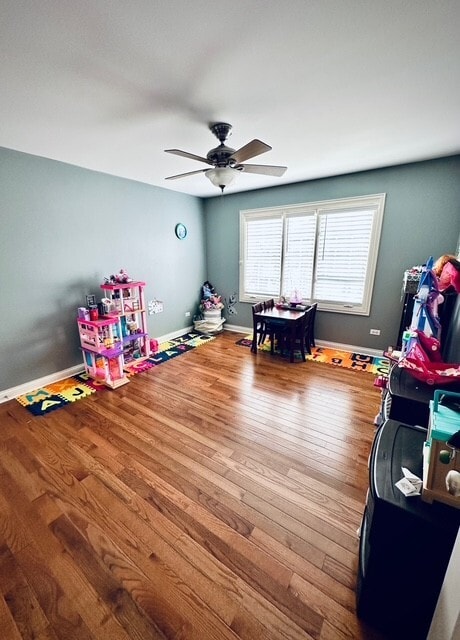 recreation room featuring wood finished floors, a ceiling fan, and baseboards