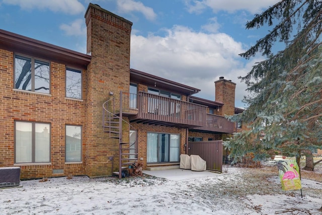 snow covered property with a chimney, stairway, a deck, central air condition unit, and brick siding