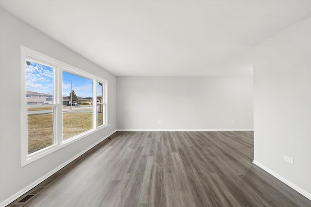 empty room with wood finished floors, visible vents, and baseboards