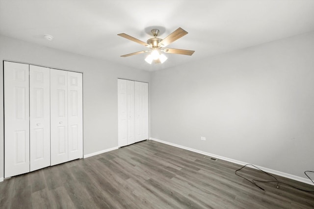 unfurnished bedroom with multiple closets, visible vents, ceiling fan, wood finished floors, and baseboards