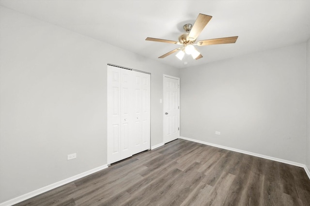 unfurnished bedroom with ceiling fan, a closet, dark wood finished floors, and baseboards