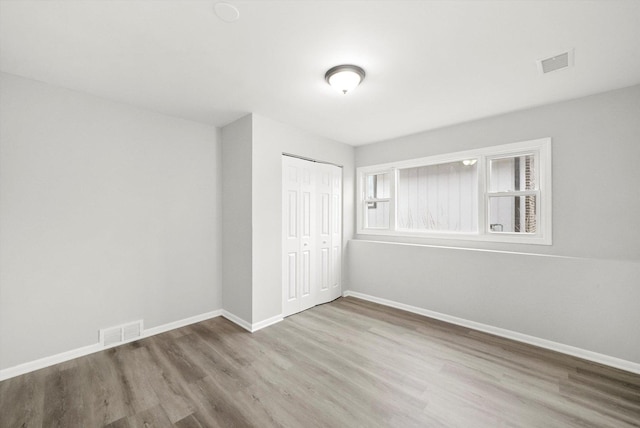 unfurnished bedroom featuring a closet, wood finished floors, visible vents, and baseboards