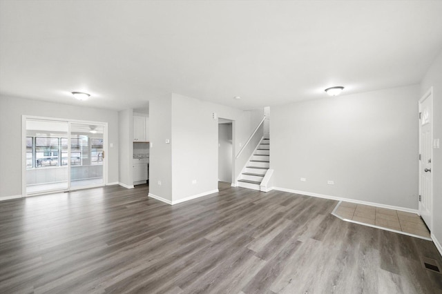 unfurnished living room with baseboards, stairway, and dark wood-style flooring