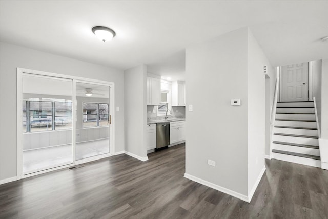 unfurnished living room featuring stairs, baseboards, dark wood-type flooring, and a sink