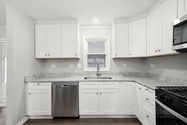 kitchen with light stone counters, appliances with stainless steel finishes, white cabinets, and a sink