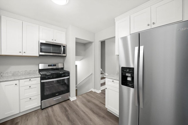 kitchen featuring light stone counters, stainless steel appliances, wood finished floors, baseboards, and white cabinets