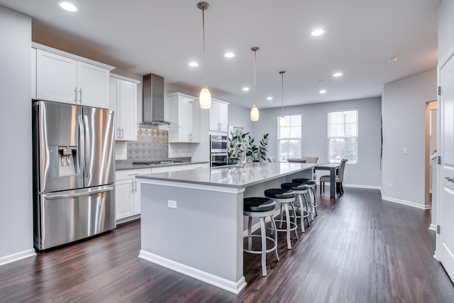 kitchen featuring a center island with sink, white cabinets, stainless steel appliances, wall chimney range hood, and backsplash