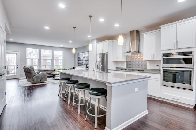 kitchen featuring tasteful backsplash, a center island with sink, stainless steel appliances, wall chimney range hood, and a sink