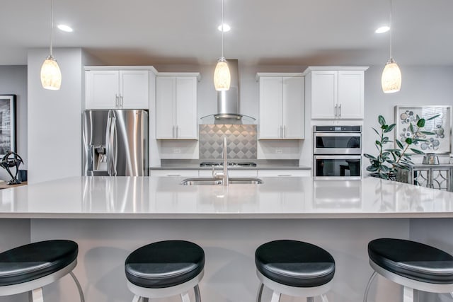 kitchen with appliances with stainless steel finishes, white cabinetry, backsplash, and wall chimney range hood