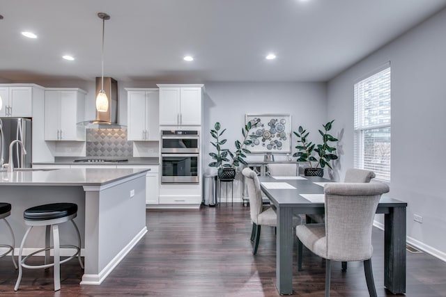 kitchen with wall chimney exhaust hood, decorative backsplash, appliances with stainless steel finishes, dark wood-type flooring, and a kitchen breakfast bar