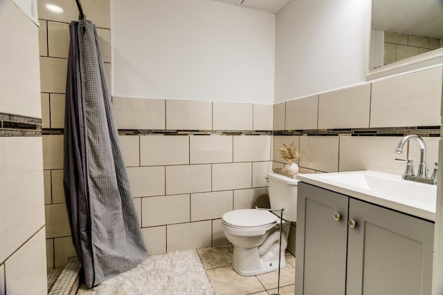 bathroom featuring toilet, tile patterned flooring, a tile shower, vanity, and tile walls