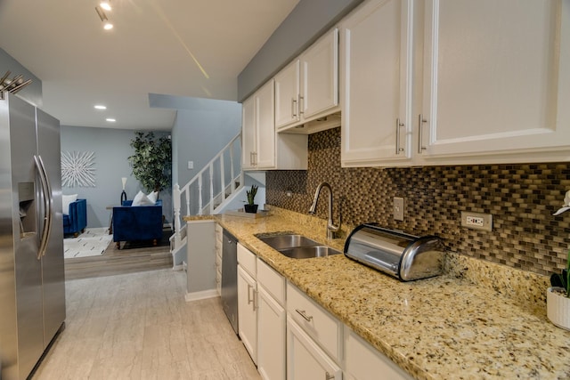 kitchen featuring light stone countertops, stainless steel appliances, a sink, light wood-type flooring, and decorative backsplash