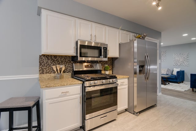 kitchen with tasteful backsplash, white cabinets, appliances with stainless steel finishes, light stone countertops, and light wood-style floors