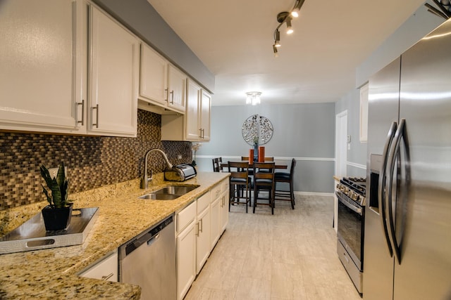 kitchen with white cabinets, appliances with stainless steel finishes, a sink, light stone countertops, and backsplash