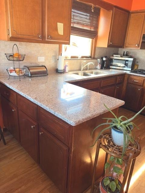 kitchen featuring a sink, decorative backsplash, light stone countertops, light wood finished floors, and stainless steel microwave