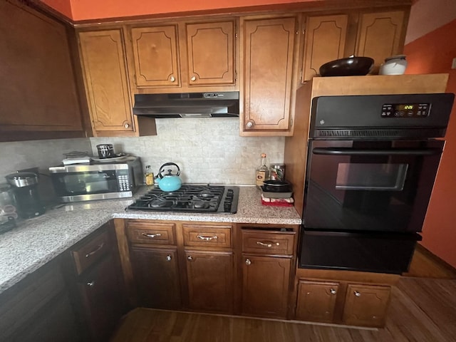 kitchen with under cabinet range hood, wood finished floors, a warming drawer, black appliances, and tasteful backsplash