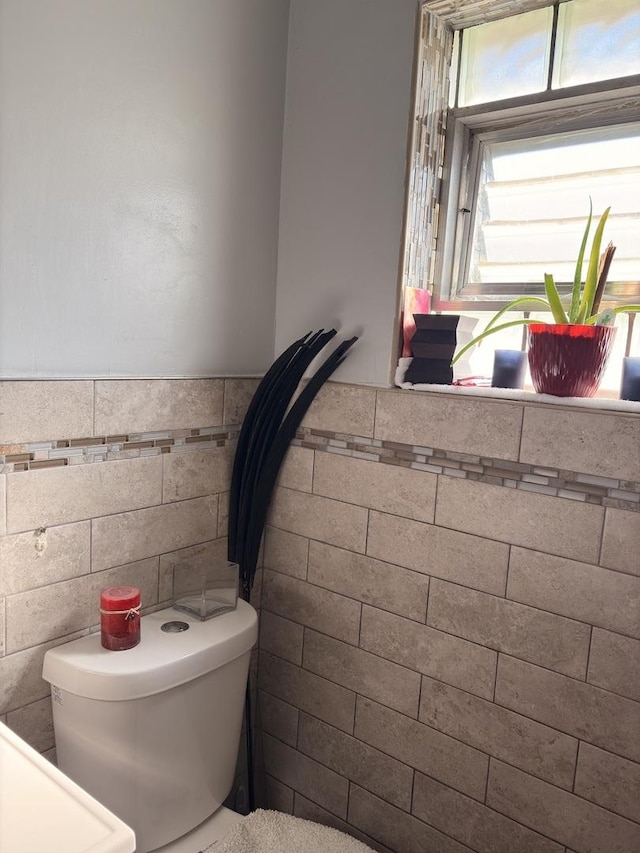 half bath featuring a wainscoted wall, tile walls, and toilet