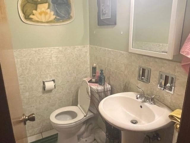 half bathroom featuring a sink, tile walls, and toilet