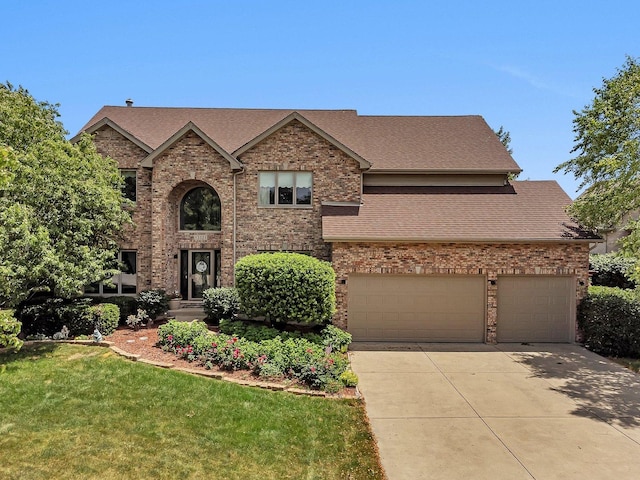 traditional-style house featuring roof with shingles, a front lawn, concrete driveway, and brick siding