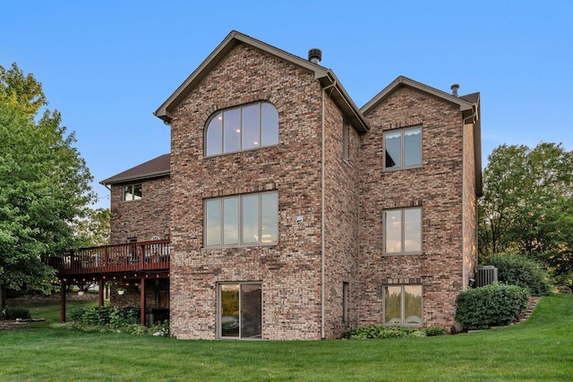 rear view of property with brick siding, a lawn, and a deck