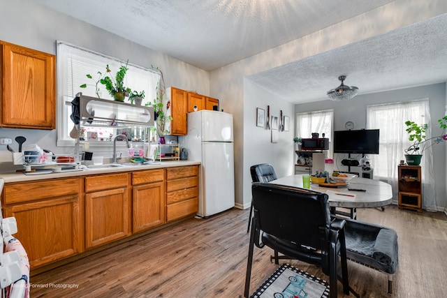 kitchen featuring brown cabinets, light countertops, freestanding refrigerator, a sink, and light wood-type flooring