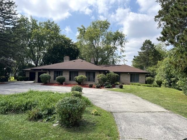 ranch-style home with driveway, an attached garage, a chimney, and a front yard