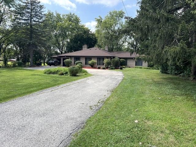 ranch-style house with driveway, a chimney, and a front yard