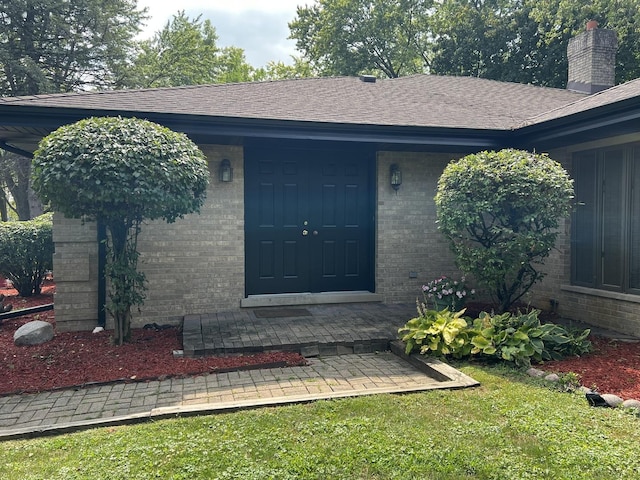 doorway to property with a shingled roof, a chimney, and brick siding