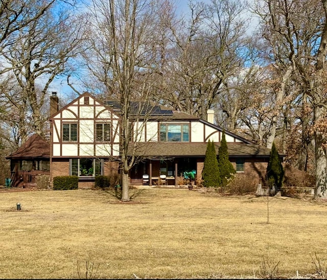 rear view of property featuring roof mounted solar panels, a lawn, and a chimney