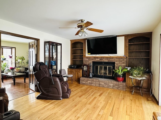 living room with a ceiling fan, a fireplace, built in features, and wood finished floors