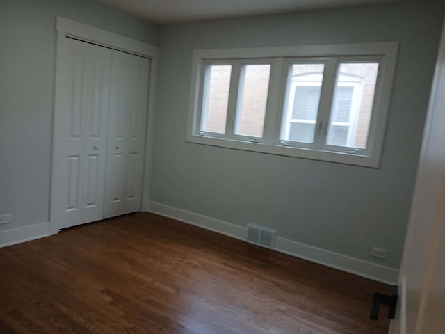 unfurnished bedroom featuring dark wood-style flooring, a closet, visible vents, and baseboards