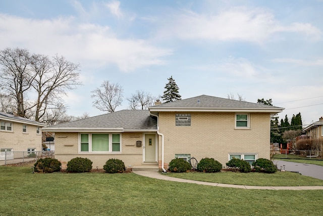 tri-level home featuring a chimney, roof with shingles, fence, a front yard, and brick siding