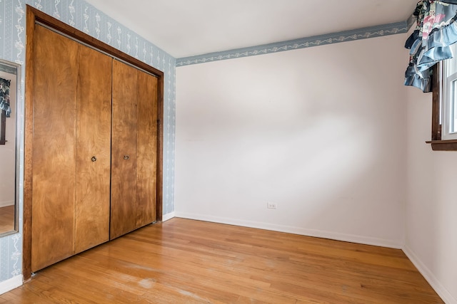 unfurnished bedroom featuring wallpapered walls, light wood-style flooring, baseboards, and a closet