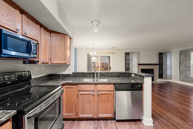 kitchen featuring a peninsula, a sink, open floor plan, appliances with stainless steel finishes, and light wood finished floors