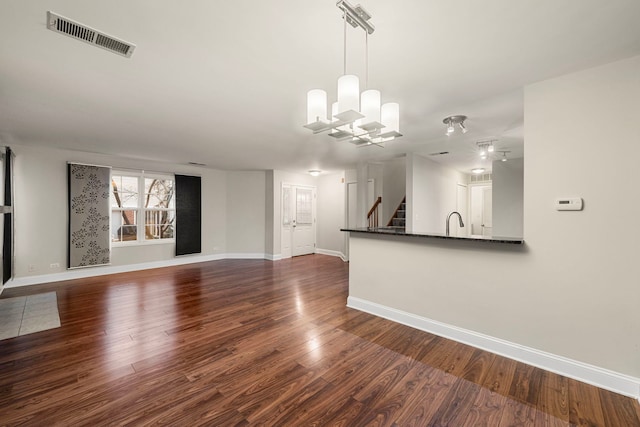 unfurnished living room featuring dark wood-style floors, visible vents, baseboards, and stairs