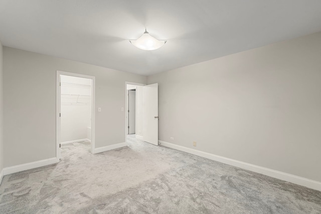 unfurnished bedroom with baseboards, a walk in closet, a closet, and light colored carpet