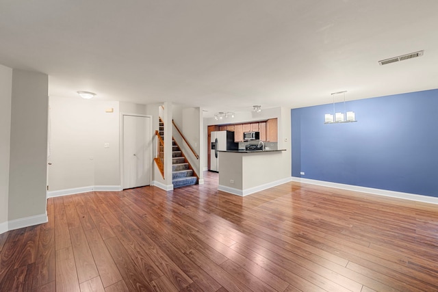 unfurnished living room with wood-type flooring, stairs, visible vents, and a notable chandelier