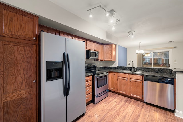 kitchen with stainless steel appliances, a sink, brown cabinets, light wood finished floors, and decorative light fixtures