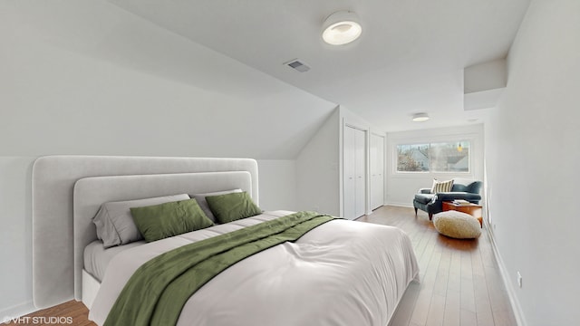 bedroom featuring lofted ceiling, visible vents, baseboards, and hardwood / wood-style flooring